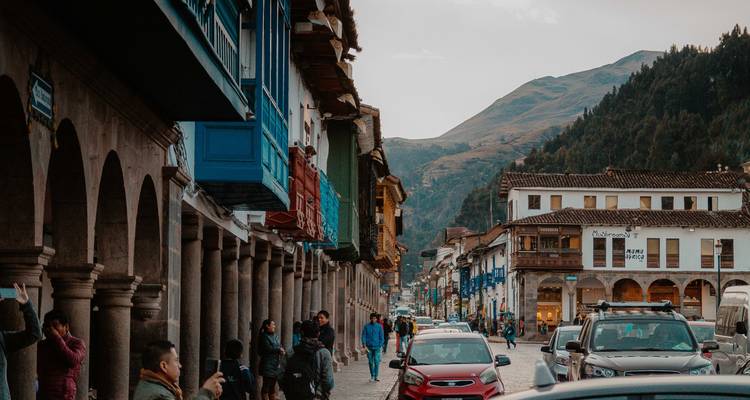 Rue coloniale animée dans une ville de montagne avec des arcades, des cafés, des voitures et des piétons au crépuscule