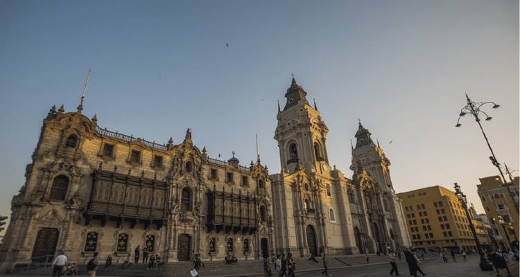 Grande cathédrale baroque et bâtiments coloniaux autour de la place principale de Lima au crépuscule avec des habitants qui se promènent.