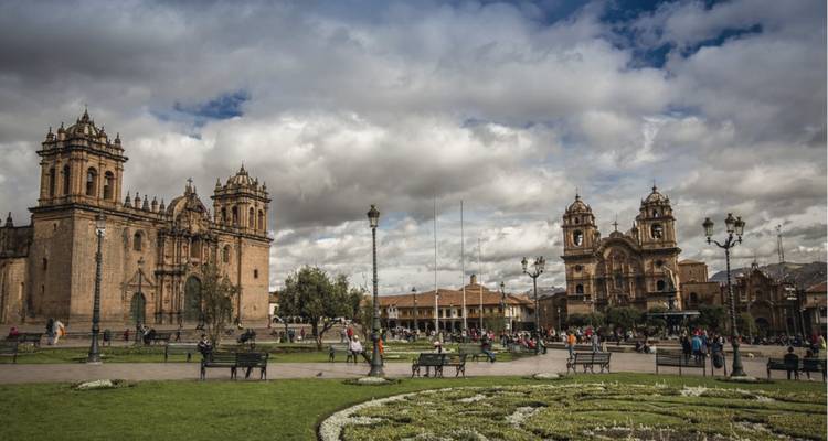 Place coloniale animée à Cusco avec cathédrales jumelles, pelouses verdoyantes et personnes se détendant.