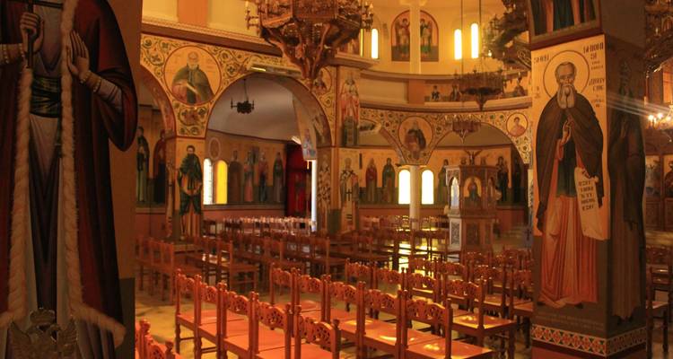 Intérieur d'une église orthodoxe richement décorée avec des chaises en bois et des fresques colorées.
