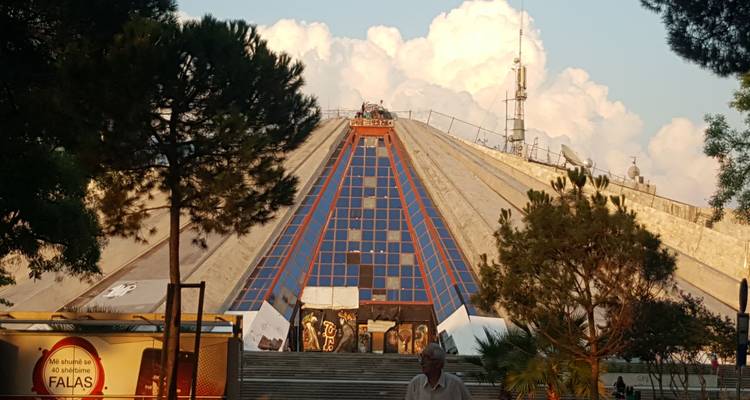 Pyramide de béton de Tirana sous une lumière de soirée chaleureuse avec des nuages en arrière-plan.