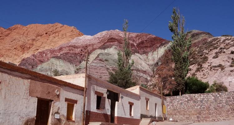 Las casas de adobe se sientan bajo las colinas de rayas arcoíris de Purmamarca contra un cielo azul brillante.