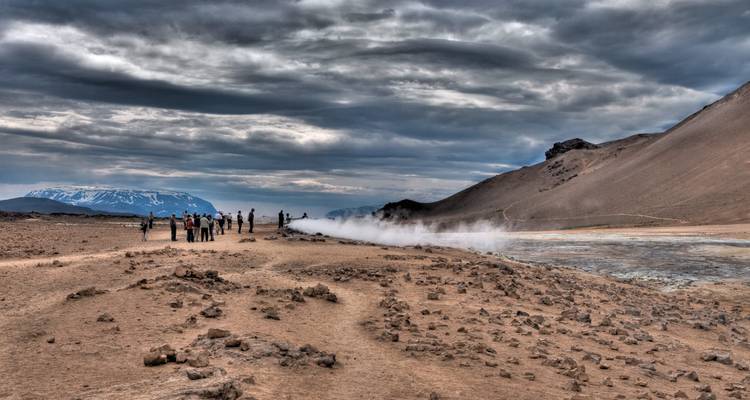 Les visiteurs regardent la vapeur s'échapper d'une plaine géothermale aride sous des nuages spectaculaires.