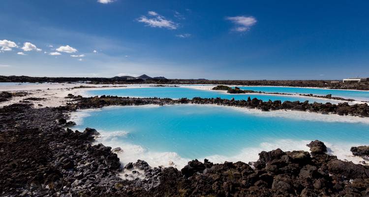 Des bassins géothermaux d'un turquoise éclatant entourés de roches volcaniques sombres sous un ciel bleu dégagé
