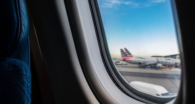Vista a través de una ventanilla de avión mostrando un jet en la pista bajo un cielo azul