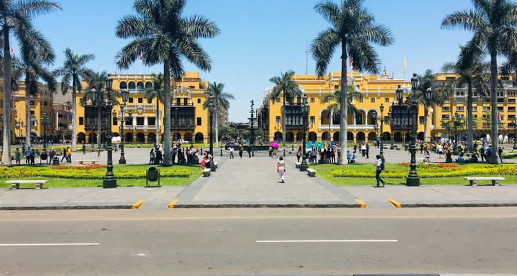 Edificios coloniales de un amarillo vibrante y palmeras rodeando la Plaza Mayor de Lima llena de gente