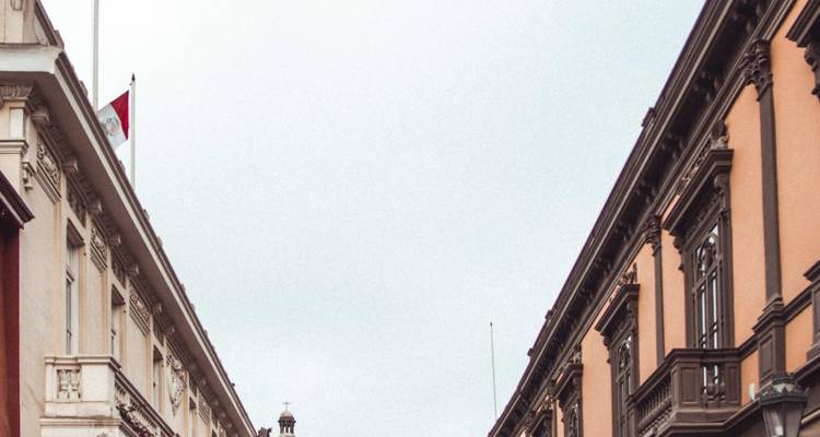 Estrecha calle histórica de Lima flanqueada por elegantes fachadas coloniales con una bandera peruana ondeando en lo alto