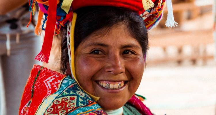 Retrato de cerca de una mujer peruana sonriente usando ropa tradicional andina colorida y un sombrero decorativo.