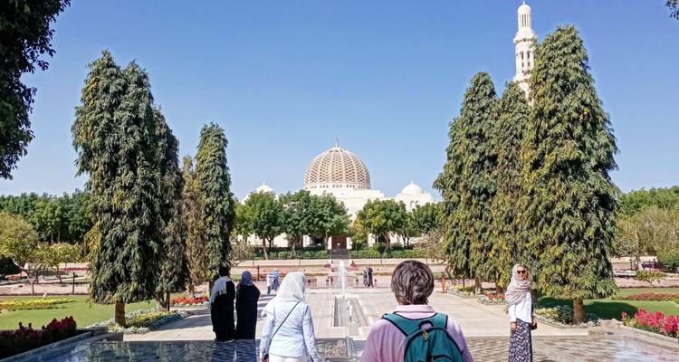 Los visitantes caminan hacia la grandiosa Mezquita del Sultán Qaboos con su cúpula blanca, enmarcada por jardines impecables.