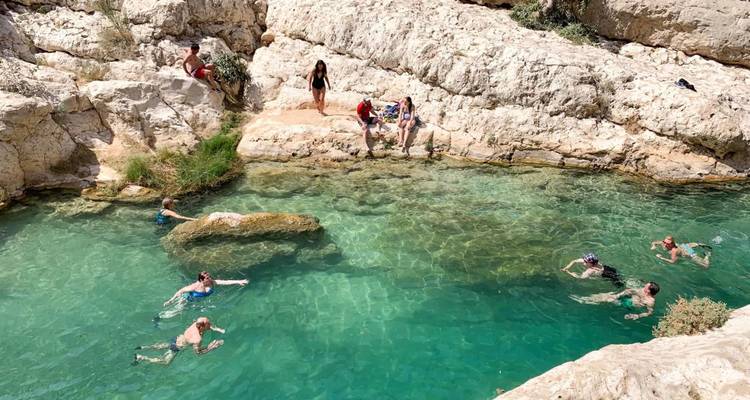 Gente nadando y relajándose en una piscina natural turquesa rodeada de paredes de cañón rocosas.