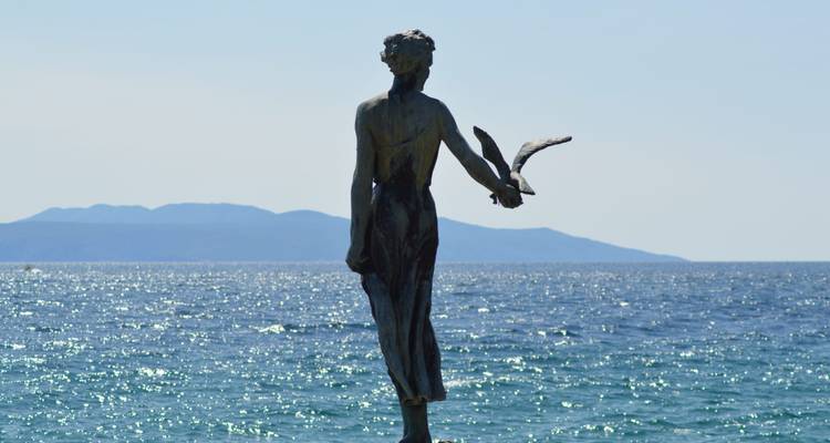 Statue de bronze en bord de mer d'une jeune fille avec une mouette dominant un panorama adriatique étincelant