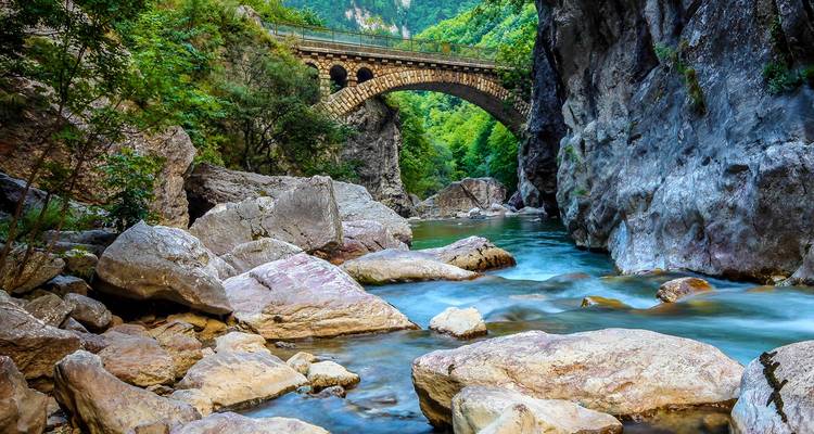 Scenic arched stone bridge spanning a turquoise river in Rugova Canyon with towering cliffs
