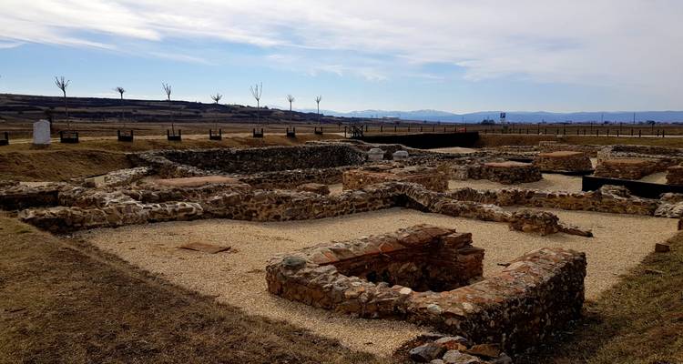 Archaeological stone foundations of an ancient settlement spread across a dry, open plain