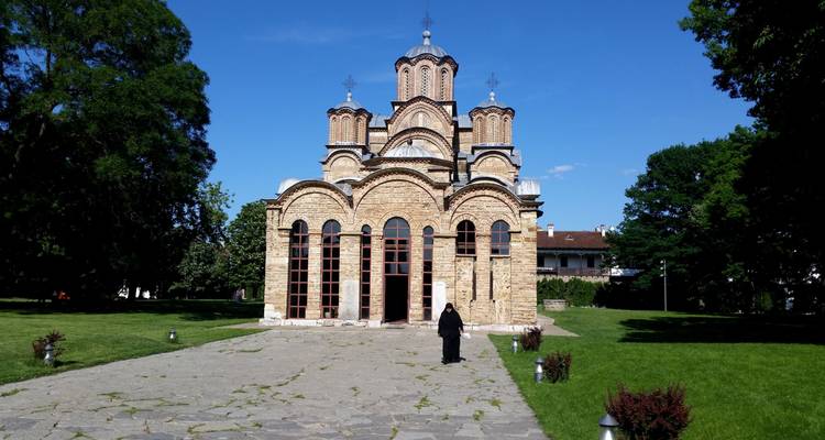 Stone Gračanica Monastery with ornate windows stands on manicured grounds under a clear blue sky