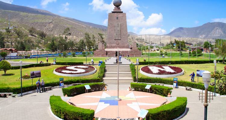 El monumento Mitad del Mundo que marca el ecuador se encuentra en un parque ajardinado bajo un cielo azul brillante cerca de Quito