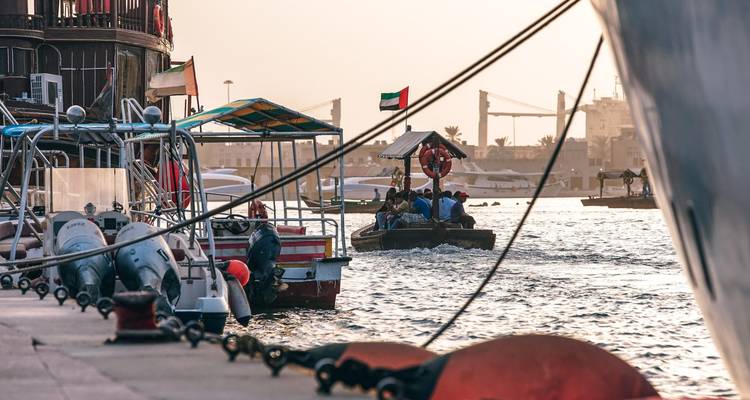 Bote abra tradicional llevando pasajeros en el Creek de Dubai al atardecer dorado con la bandera de los EAU ondeando.