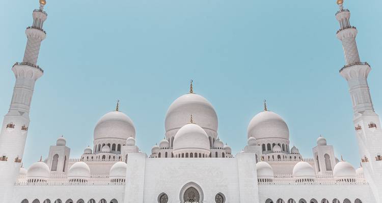 Vista cercana y simétrica de las cúpulas blancas de la Gran Mezquita del Jeque Zayed enmarcadas por dos minaretes elevados contra un cielo de tonos pastel.
