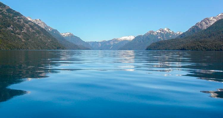 Stiller blauer See, der schneebedeckte Berge unter klarem Himmel widerspiegelt.