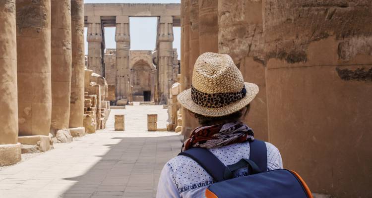 Voyageur portant un chapeau de paille et un sac à dos marchant entre les imposantes colonnes de grès du Temple de Louxor