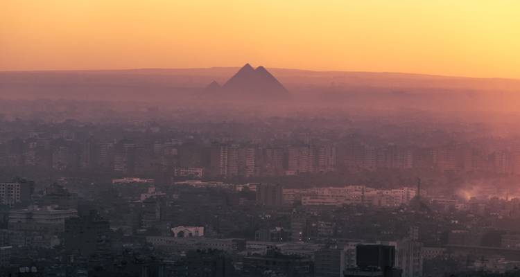 Vue du coucher de soleil brumeux sur l'horizon du Caire avec la silhouette lointaine des pyramides de Giza émergeant de la brume