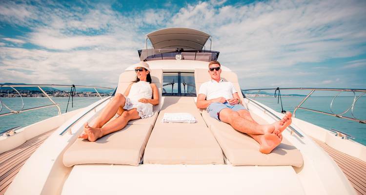 Homme et femme prenant un bain de soleil sur le pont d'un yacht de luxe sous un ciel partiellement nuageux.