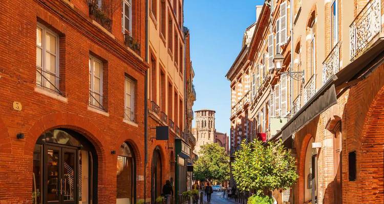 Ruelle étroite en briques rouges avec commerces et jardinières plantées de verdure dans la vieille ville de Toulouse.