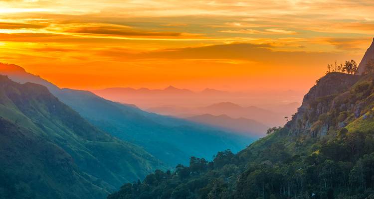 Levendige zonsondergang die oranje en roze tinten over een mistig bergdal in Sri Lanka werpt.