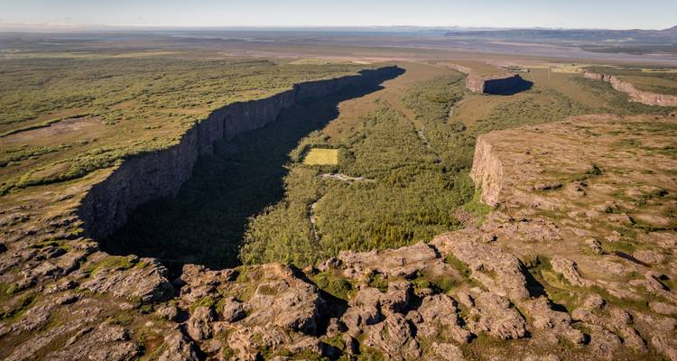 Luchtfoto van de hoefijzervormige kliffwanden van de Asbyrgi-canyon met dicht bos en een grazig dal erin.