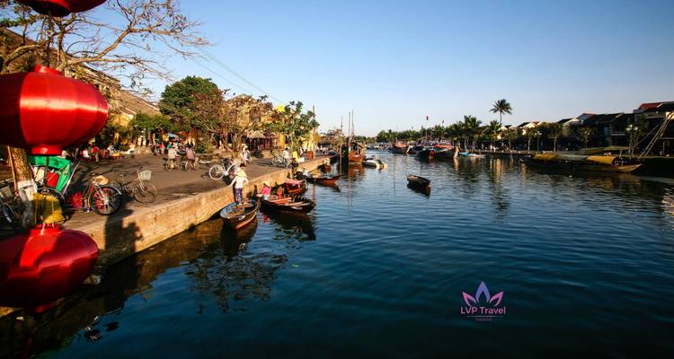 Rivieroever scène met boten en lantaarns in Hoi An met logo watermerk van touroperator.