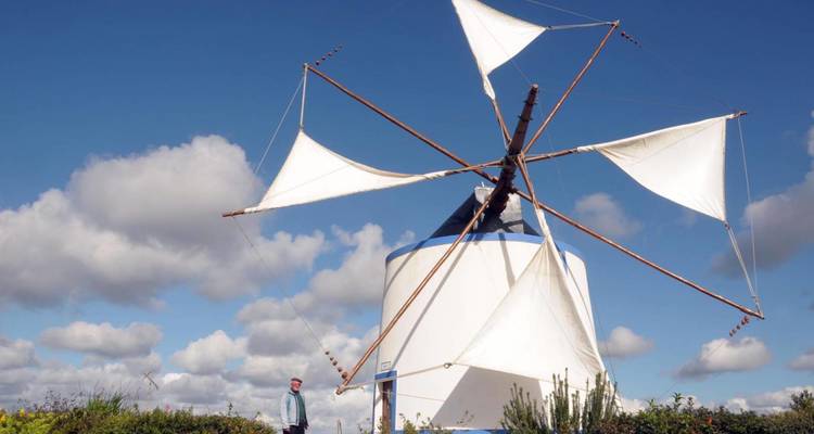 Traditional white windmill with cloth sails turning under a blue sky dotted with clouds.