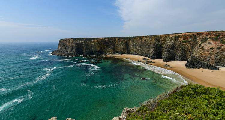 Turquoise waters lap dramatic sea cliffs and a secluded sandy beach on the Atlantic coast.