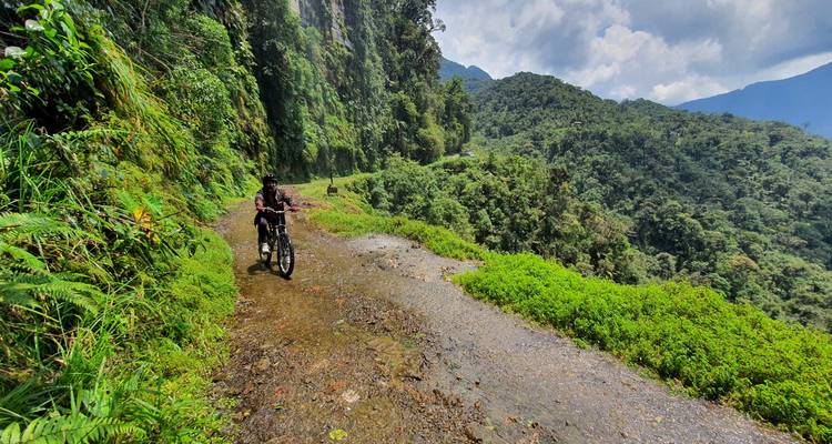 Mountainbiker die langs een smal nat pad door dichte groene jungle rijdt op Death Road