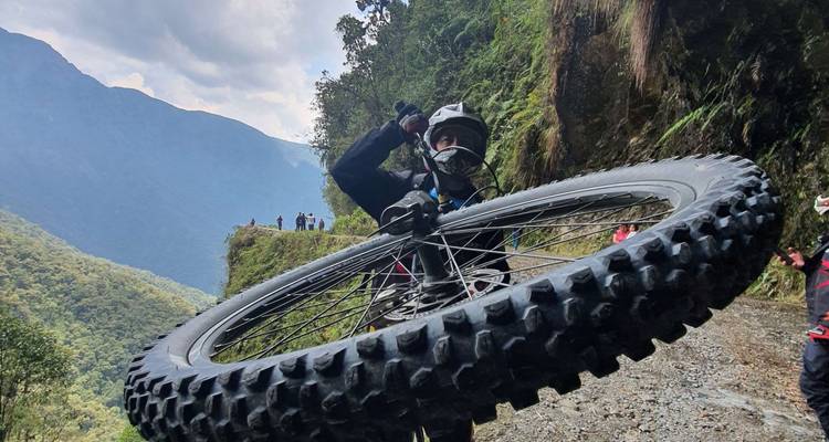 Mountainbiker die een knobbelwiel naar de camera tilt op een bergpaadje aan de rand van een klif