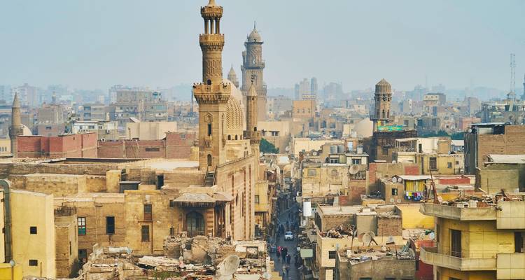 Dicht opeengepakte skyline van het historische islamitische Caïro met uittorenende minaretten en stoffig nevel