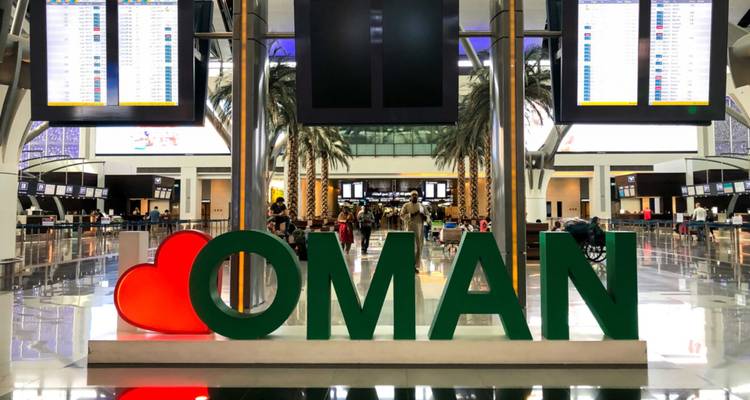 Intérieur de l'aéroport international de Mascate avec une grande icône de cœur et des lettres OMAN vertes, des palmiers et des comptoirs d'enregistrement en arrière-plan