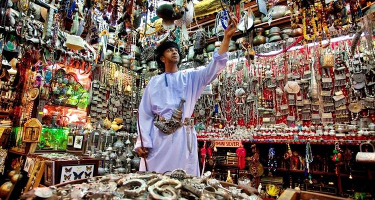 Homme vêtu d'une tenue traditionnelle omanaise consultant un étal de souq vibrant rempli de bijoux en argent et de bibelots colorés