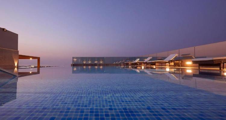 Infinity rooftop pool reflecting twilight sky with sun loungers lined along glass panels
