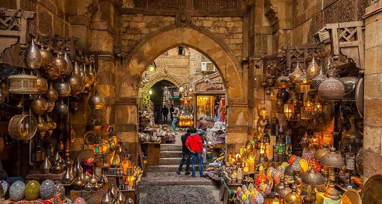 Une ruelle animée du bazar historique du Caire illuminée par des lanternes, encadrée par une arcade en pierre.