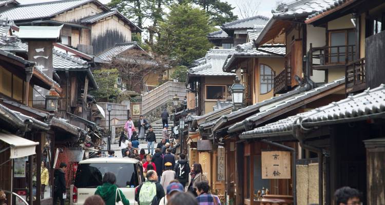 Drukke traditionele straat in Kyoto vol met houten huizen, winkels en wandelende bezoekers.