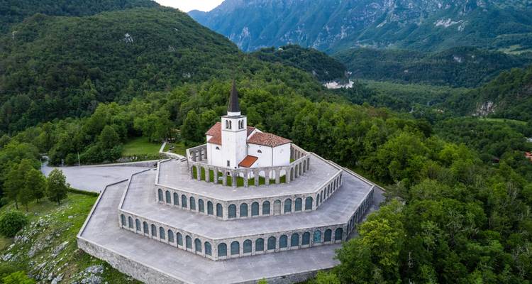 Vue aérienne par drone d'une église commémorative circulaire en terrasses entourée d'une forêt dense et verdoyante dans la vallée de la Soča.