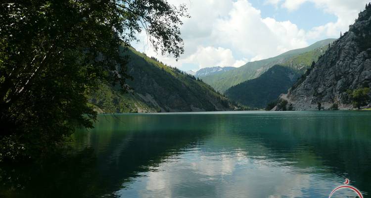 Ruhiger smaragdgrüner See, umgeben von steilen bewaldeten Hängen, die sich im stillen Wasser spiegeln.