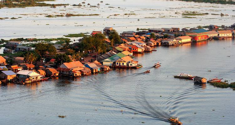 Farbenfrohe Pfahlbauten bilden ein schwimmendes Dorf auf dem Tonle Sap, während Boote kräuselnde Kielwasser hinterlassen.