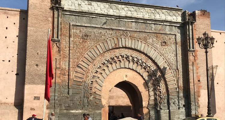 Puerta de la ciudad con arcos ornamentados decorada con tallas intrincadas y una gran bandera marroquí