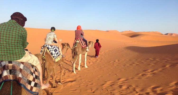 Caravana de viajeros cabalgando camellos a través de dunas de arena ondulantes al amanecer