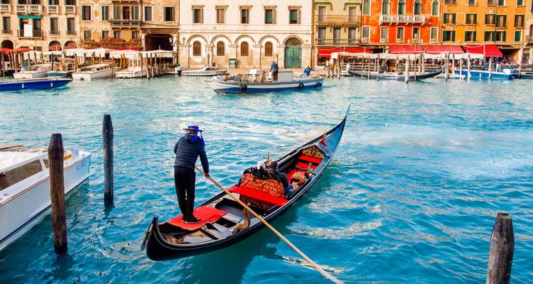 Un gondolier propulse une gondole traditionnelle le long du Grand Canal de Venise avec des palais ornés en arrière-plan.