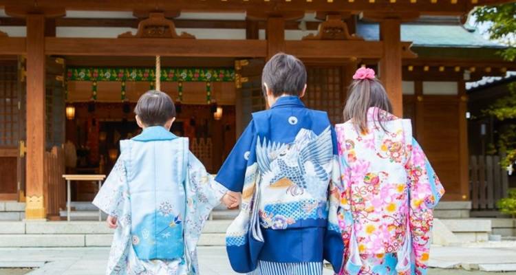 Drie kinderen in kleurrijke kimono's lopen hand in hand naar de ingang van een Shinto-heiligdom.