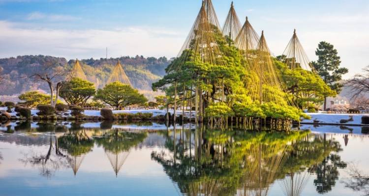Reflejos de islas rodeadas de pinos en un estanque tranquilo del Jardín Kenroku-en con soportes de cuerda invernal en los árboles