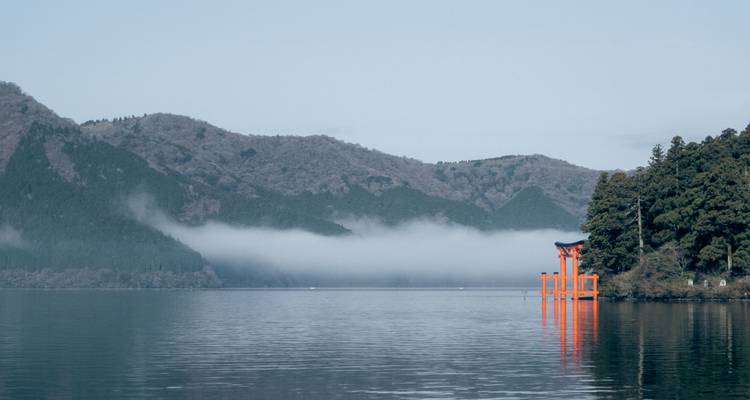 Der ruhige See Ashi mit fernem Torii-Tor und leichtem Nebel, der die bewaldeten Berge umhüllt