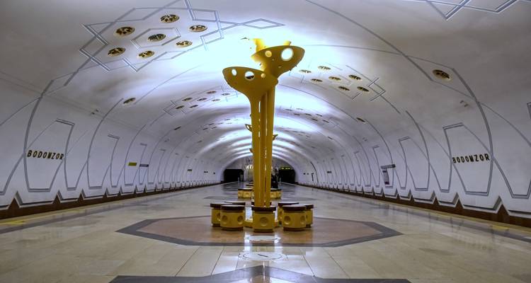 Futuristic empty platform of Tashkent’s Bodomzor metro station with bright yellow central sculpture.