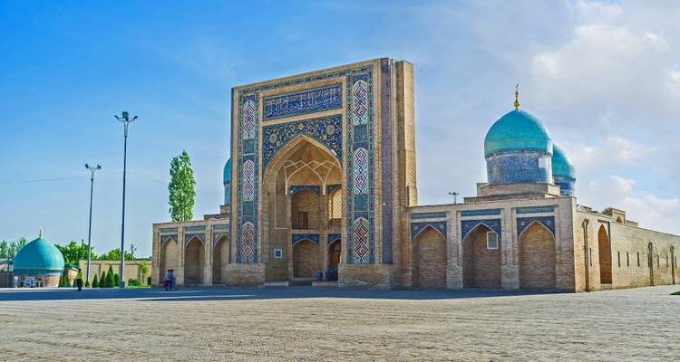Barak-Khan Madrasah complex with ornate tiled portal and turquoise domes in spacious courtyard.